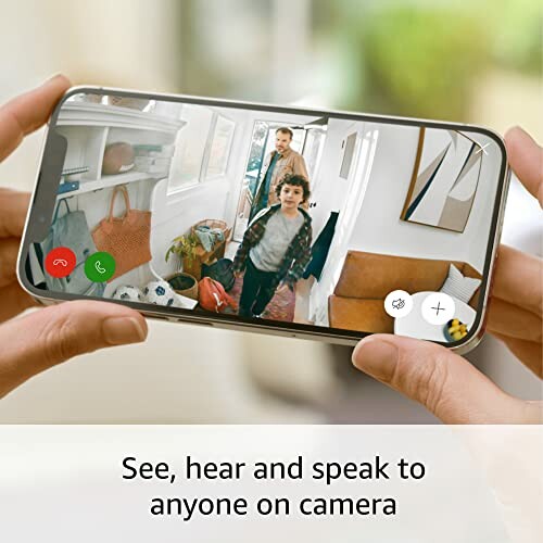 Person holding smartphone showing video call with two people entering a house